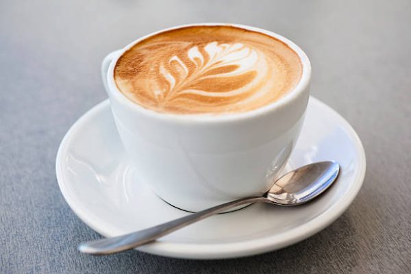 A flat white coffee with leaf pattern on grey background. More coffee